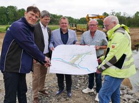 Vertreter des Zweckverbands Hochwasserschutz mit Bürgermeister und Oberbürgermeister halten den Plan zum neuen Hochwasserrückhaltebecken